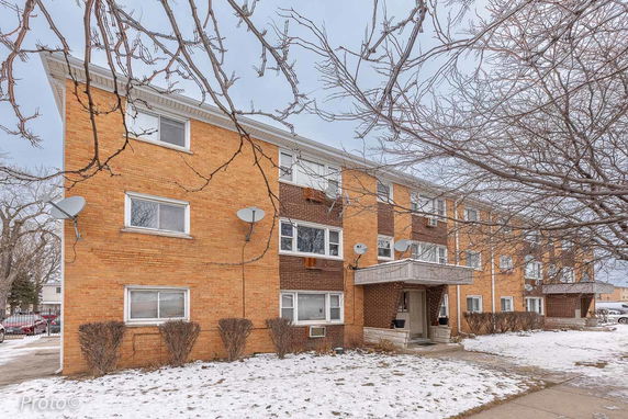 Front view of a three-story brick apartment building with multiple windows and satellite dishes.