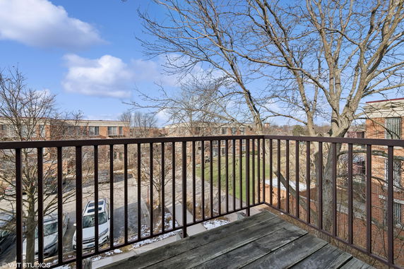 View from a balcony overlooking apartment buildings and a parking area with a clear blue sky.
