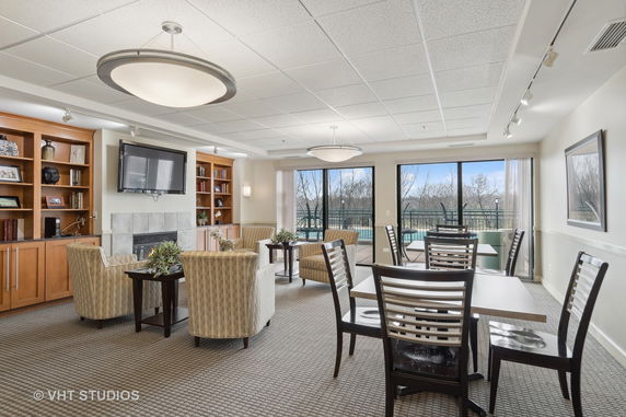 Lounge area with chairs, tables, a fireplace, and a TV in a clubhouse setting.