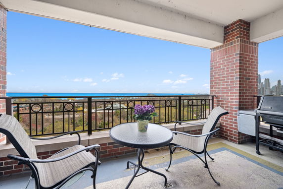 Outdoor balcony with a glass table and chairs overlooking a city and ocean.