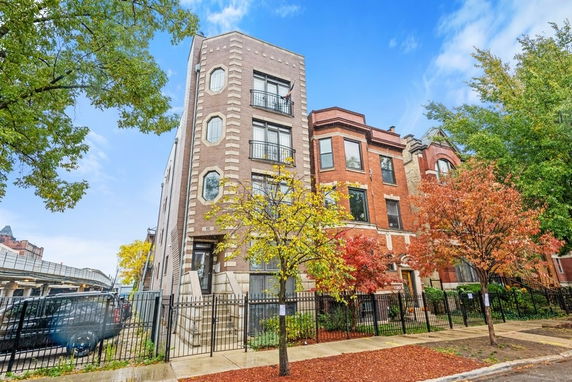 Front view of a row of multi-story brick buildings with black railings and a fenced front yard.