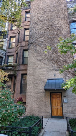 Front view of a multi-story brick building with a wooden door and vines on the facade.