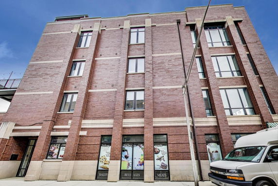 Front view of a multi-story brick building with tall windows and storefronts on the ground level.