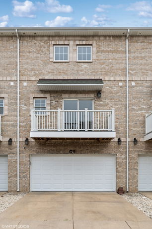 Front view of a multi-story townhouse with a balcony over a double garage.