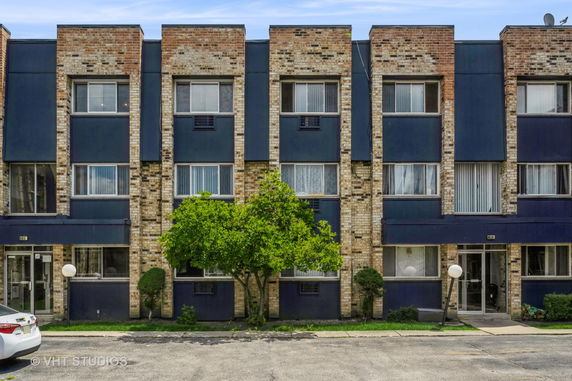Front view of a three-story apartment building with a brick facade and multiple windows.