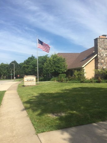 Front view of a house with stone chimney and American flag on lawn.