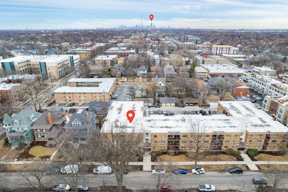 Aerial view of a residential area with multiple buildings and houses, featuring a city skyline in the distance.
