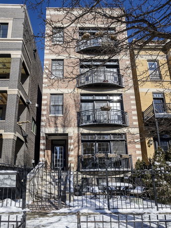Front view of a multi-story brick building with balconies and a gated entrance.