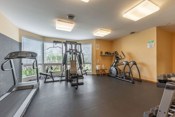 Interior view of a gym area with exercise equipment and large windows.