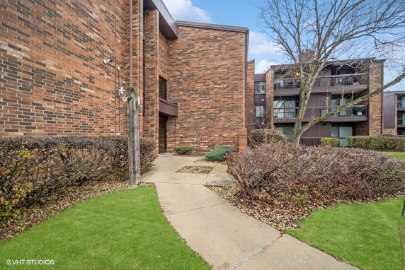 Front view of a brick apartment building with balconies and landscaped surroundings.
