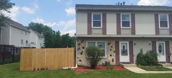 Front view of a two-story duplex building with a wooden fence and garden area.