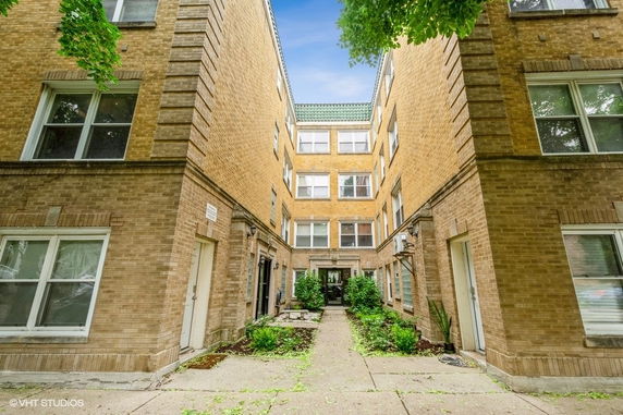 Front view of a multi-story brick apartment building with a courtyard entrance.