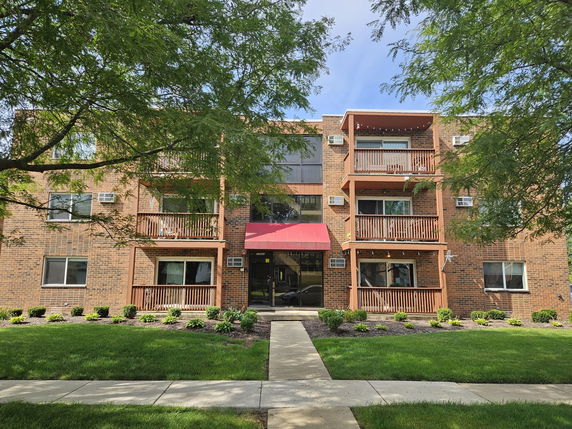 Front view of a three-story brick apartment building with balconies.