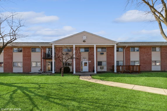 Front view of a two-story apartment building with red brick facade and white columns.