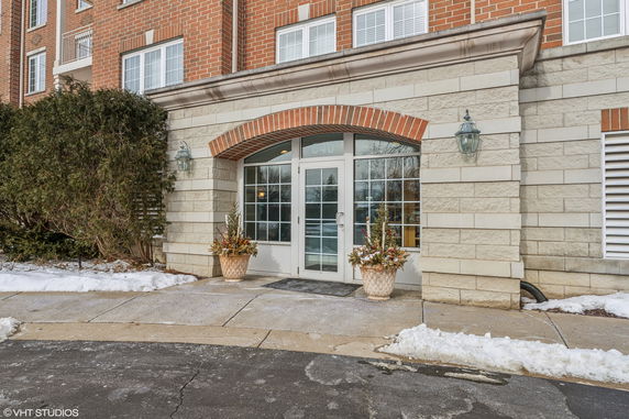 Front view of a multi-story building entrance with large glass doors and decorative brickwork.