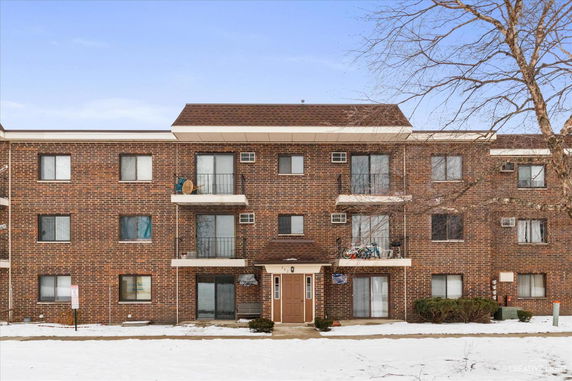 Front view of a three-story brick apartment building with balconies.