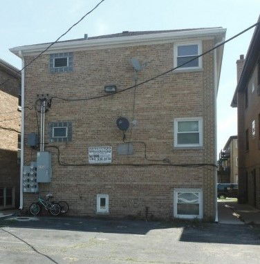 Rear view of a three-story brick building with several satellite dishes and cables attached.