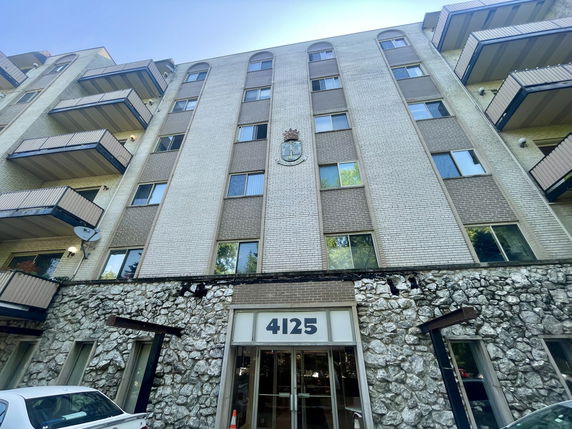 Front view of a multi-story building with balconies and a textured stone entrance.