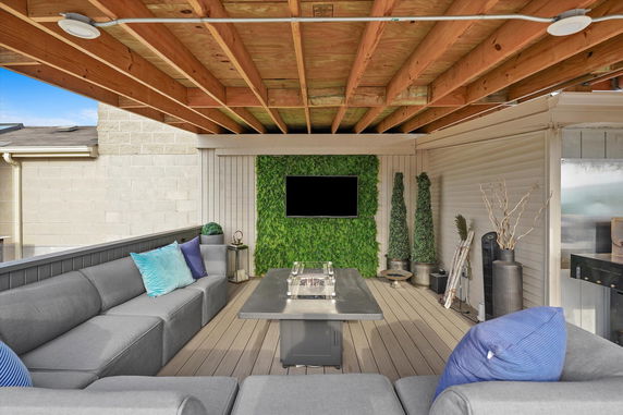 Covered rooftop seating area with a TV, green wall, and modern furniture.
