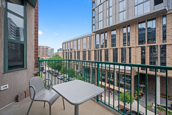 View from a balcony overlooking modern apartment buildings and a street with trees.