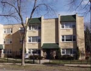 Front view of a three-story apartment building with green awnings and a fenced front yard.