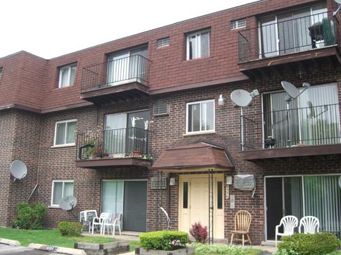 Front view of a three-story apartment building with balconies and a brown shingled roof.