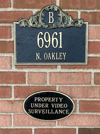 Brick wall with an address plaque and surveillance warning sign.