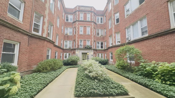 Front view of a multi-story brick apartment building with lush greenery.