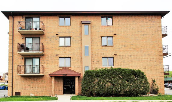 Front view of a four-story brick apartment building with balconies.