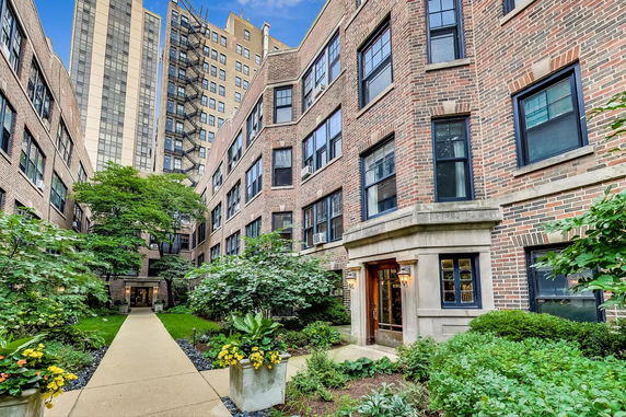 Front view of a multi-story brick apartment building with landscaped courtyard.