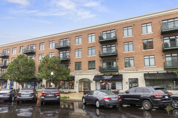 Front view of a multi-story brick building with balconies and a ground floor dedicated to retail space.
