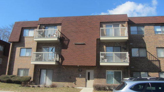 Front view of a three-story brick apartment building with balconies.