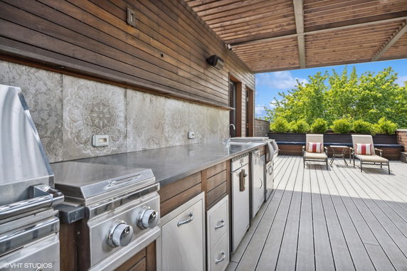 Rooftop with a wooden deck, outdoor kitchen, and lounge chairs.