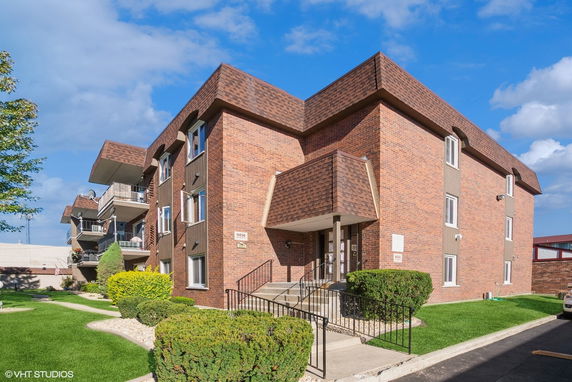 Front view of a multi-story brick building with balconies and landscaped surroundings.