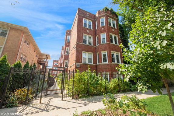 Front view of a multi-story brick apartment building with multiple windows and a gated entrance.