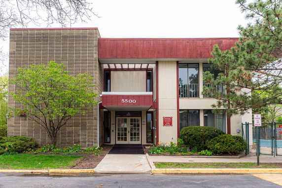 Front view of a two-story building with a red and beige facade and glass entrance.