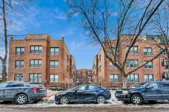 Front view of adjacent brick apartment buildings with multiple windows and parked cars in front.