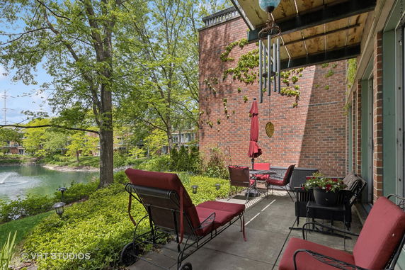Outdoor patio area with seating furniture and view of a lake surrounded by trees and buildings.
