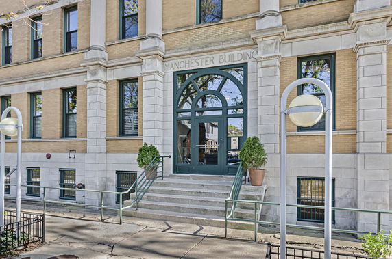 Front view of a multi-story brick building with arched entrance and steps.