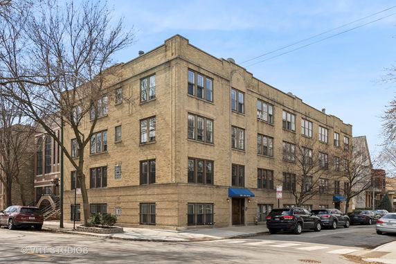 Front view of a four-story apartment building with brick exterior and blue awnings over the entrances.