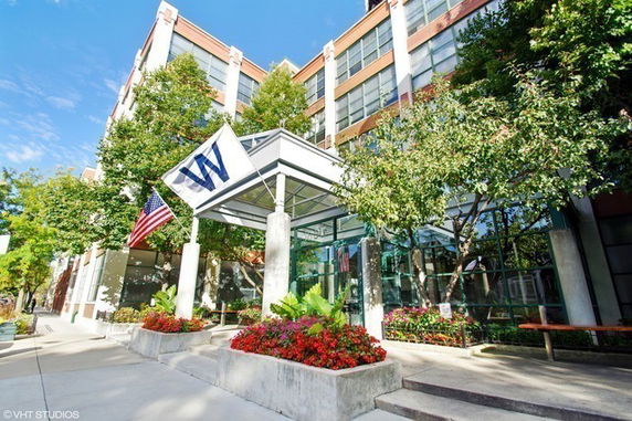 Front view of a modern multi-story building with glass and concrete structure, featuring flags at the entrance.