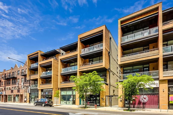 Front view of a modern multi-story building with prominent balconies and retail spaces on the ground floor.