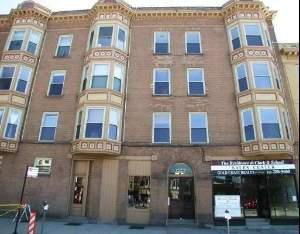 Front view of a multi-story brick building with bay windows and ground-level shops.