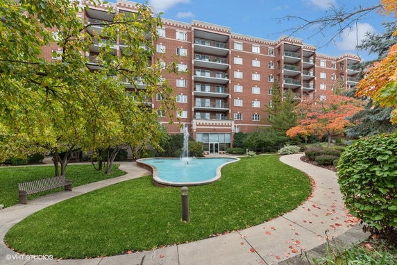 Front view of a multi-story brick residential building with balconies and a garden with a fountain.
