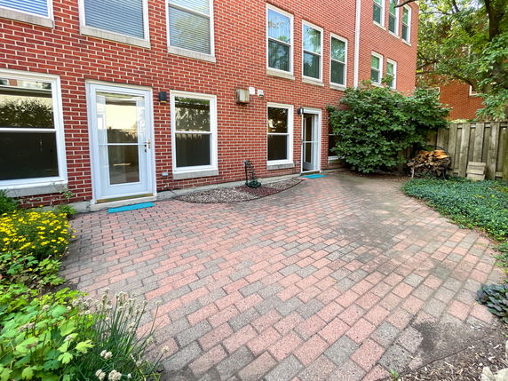 Back view of a brick building with multiple windows and a glass door leading to a patio area.