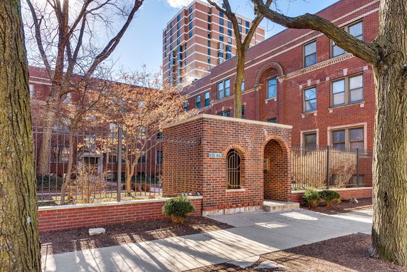 Front view of a brick multi-story building with arched entrance and wrought iron fencing.
