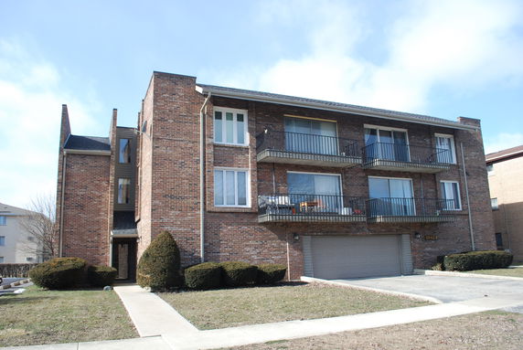Front view of a multi-story brick building with balconies and a garage.