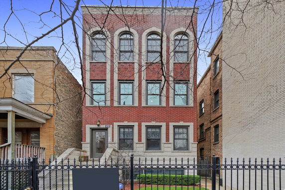 Front view of a three-story red brick building with large windows.