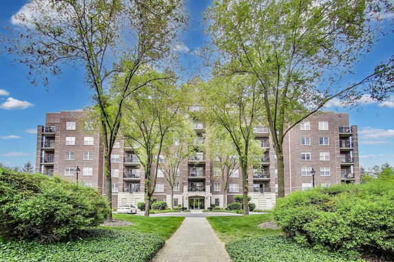 Front view of a multi-story brick building with balconies and surrounding trees.