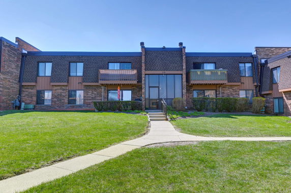 Front view of a two-story apartment building with balconies and stairs leading to the entrance.